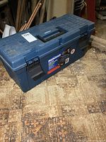 Closed Mastercraft 25" blue plastic toolbox on a patterned floor showing latches and handle