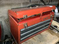 Front view of red Craftsman metal toolbox with drawers and top storage compartment, showing wear and rust.