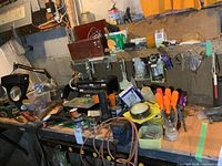 View of workbench with 3-inch blue bench vise, assorted hand tools, flashlights, extension cords, and hardware containers