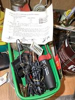 Red-handled propane torch with cords and hardware in green tray on workbench