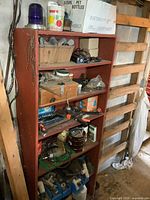 Full view of the red wooden shelf filled with assorted tools, hardware, pipe fittings, power tools, and boxes.