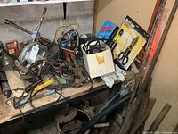 Workbench and shelf with assorted hand and power tools including circular saw, braces, pliers, nail pullers, hand tools in box, scissors in plastic packaging.