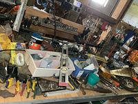 Wide view of workbench showing various hand tools including screwdrivers, clamps, sockets, and hardware containers scattered on surface.