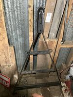 Full view of black steel triangular tow bar standing vertically against wooden and metal background