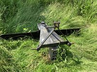 Full view of scraper blade and triangular hitch frame resting on concrete block in grass