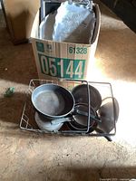 Box containing metal basket filled with various sizes of metal pots along with some other pots outside the basket.