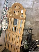 Four wooden trellis panels leaning against a concrete block wall in a storage area. One panel has a painted upper decorative circular element, others are natural wood.