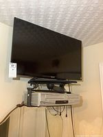 Sony 32 inch flat screen TV mounted on wall with platform mount, showing front view with Sylvania combo DVD/VHS player beneath.