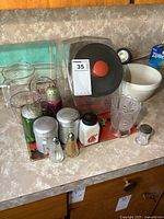 Wide view of the lot showing glass canister, stoneware bowl, measuring cups, various shakers, and glass tumbler on countertop.