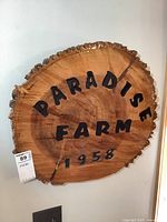 Front view of the wood sign showing engraved 'PARADISE FARM 1958' on a natural wood slice with bark edges.