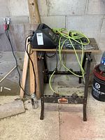 View of Jobmate work stand with battery charger, work light cord, and large screwdriver on and around it in a garage setting
