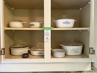 Cabinet shelf showing eight CorningWare pieces with lids