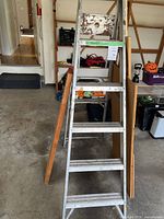 Full view of aluminum step ladder with scrap wood leaning against it