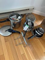 Group of cookware on floor including Presto pressure cooker, lid, nested pans, racks