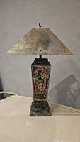 Front view of the bronze and black metal table lamp showing the tribal relief on the body and the bronze metal shade with triangular cutouts.