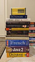Books stacked showing titles and authors, including a yellow book with Asian characters on top and various English language books including a dictionary and programming guides.