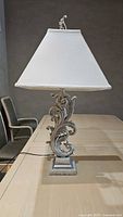 Full side view of the decorative lamp on a table with white fabric shade and ornate metal base.