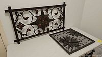 Two metal wall art panels with floral designs, one rectangular and one square, placed on a white surface.