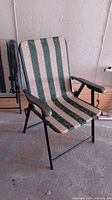 Single foldable patio chair in green and beige stripes, showing front view with armrests and black metal frame