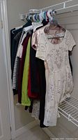 View of various women's clothes hanging on a closet rod, including a white/beige patterned dress in front.