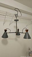 Full view of the chandelier hanging, showing the three conical gray metal shades and wood tone accents, with a wired suspension system.