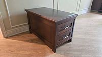Side angle view of a modern solid wood storage chest with two drawers and brown finish.