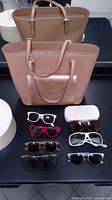 Michael Kors pink tote handbag and six pairs of sunglasses arranged on a dark surface.