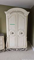 Front view of the closed beige wooden Pulaski armoire wardrobe with carved floral top and round drawer pulls.