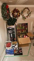 Full view of the seasonal decorative items including wreaths hung on the wall and boxes of ornaments and lights on the floor.