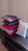 Stack of six pillows on wooden bench, various colors and fabrics