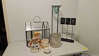 Table display of all items including the glass terrarium, ceramic doll, ceramic floral containers, tall candle holder, and foliage sign holder