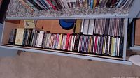 Drawer filled with approximately 45 CDs in plastic jewel cases, arranged horizontally.