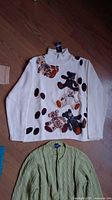 White knit sweater with teddy bear designs and brown spots on a wooden floor.