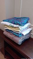 Stack of folded linen pieces in various colors and prints on wooden furniture