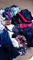 Photo showing a pile of assorted women's vintage and modern clothing including floral tops, knitwear, and jackets in various colors.