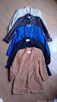 Five women's blazers in colors light beige, dark gray, blue and black, navy blue, and brown with textured fabric.
