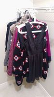 Various women's clothing items on hangers including a black sleeveless dress and southwestern pattern sweaters.