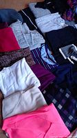 Multiple folded sweaters and tops in various colors including grey, black, pink, and striped patterns.
