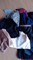 Clothing items laid out on floor showing variety of tops including knit, patterned, white shirt and blue jacket