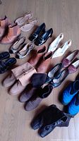 Top view of 14 pairs of various women's shoes arranged on wooden floor including boots, heels, flats, slip-ons.