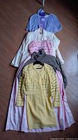 Lot of five women's vintage clothing items laid out on the floor including dresses and jackets in various pastel shades.