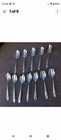 Full set of 12 Oneida Queen Bess II silverplate teaspoons laid out on a dark cloth surface.