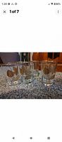 Five clear highball glasses with gold leaf designs arranged on carpet