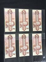 Six Canadian $2 banknotes front side with Queen Elizabeth II portrait visible in protective sleeves