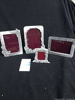 Four pewter picture frames displayed on black fabric background, showing general appearance and four sizes including three 4x6 inch and one 2x2 inch frame with floral designs.