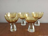 Front view of five amber-colored martini glasses with clear stems arranged in a group on a wooden surface.