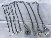 Front view of 8 necklaces laid flat, showing variety of pewter pendants on black rope and metal ball chains