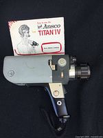 Side view of the Ansco Titan IV vintage 8mm movie camera with instruction manual in background.
