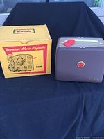 Brownie 8mm movie projector in brown carrying case with original yellow Kodak box beside it