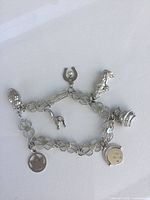 Full view of silver metal charm bracelet with seven distinct charms displayed on white background.